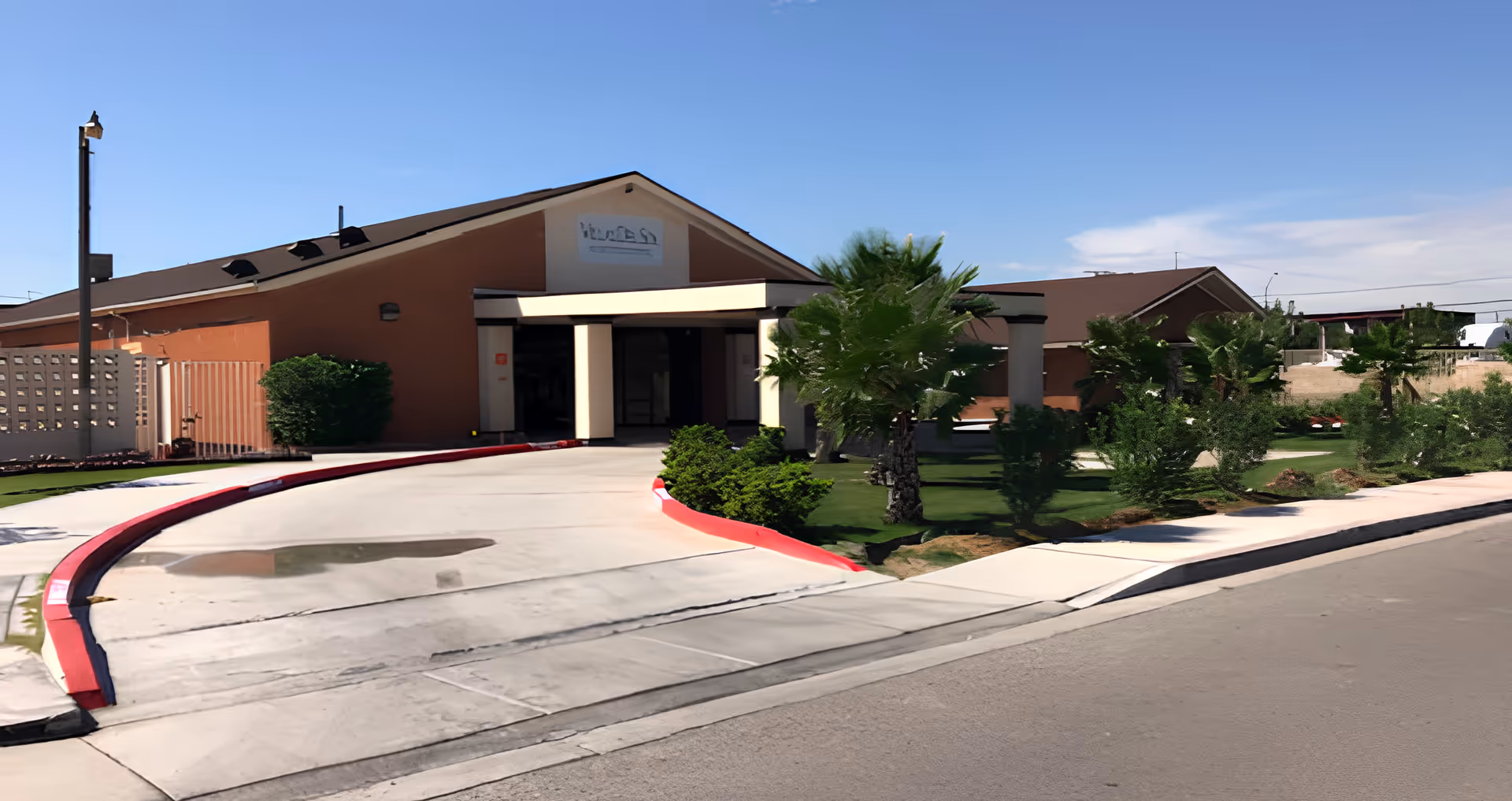 Front entrance of Villas Del Sol Assisted Living showing a curved driveway, covered entry, and landscaped lawn.