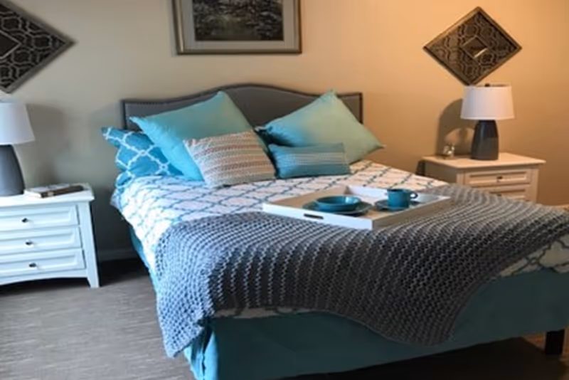 A cozy bedroom featuring teal bedding, decorative pillows, and white nightstands with lamps.