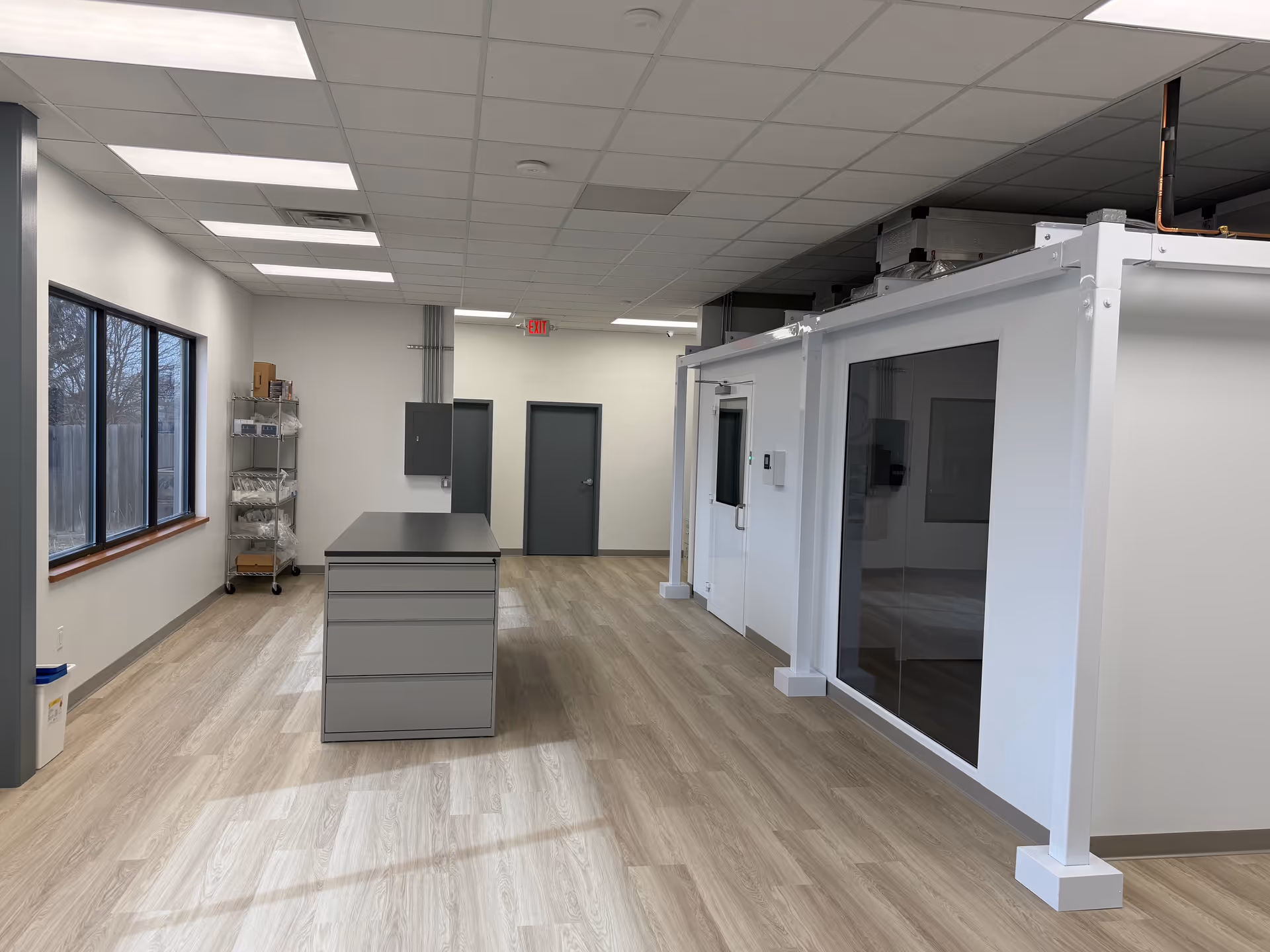 Bright, modern medical facility interior featuring a central island, glass-walled room, and shelves.