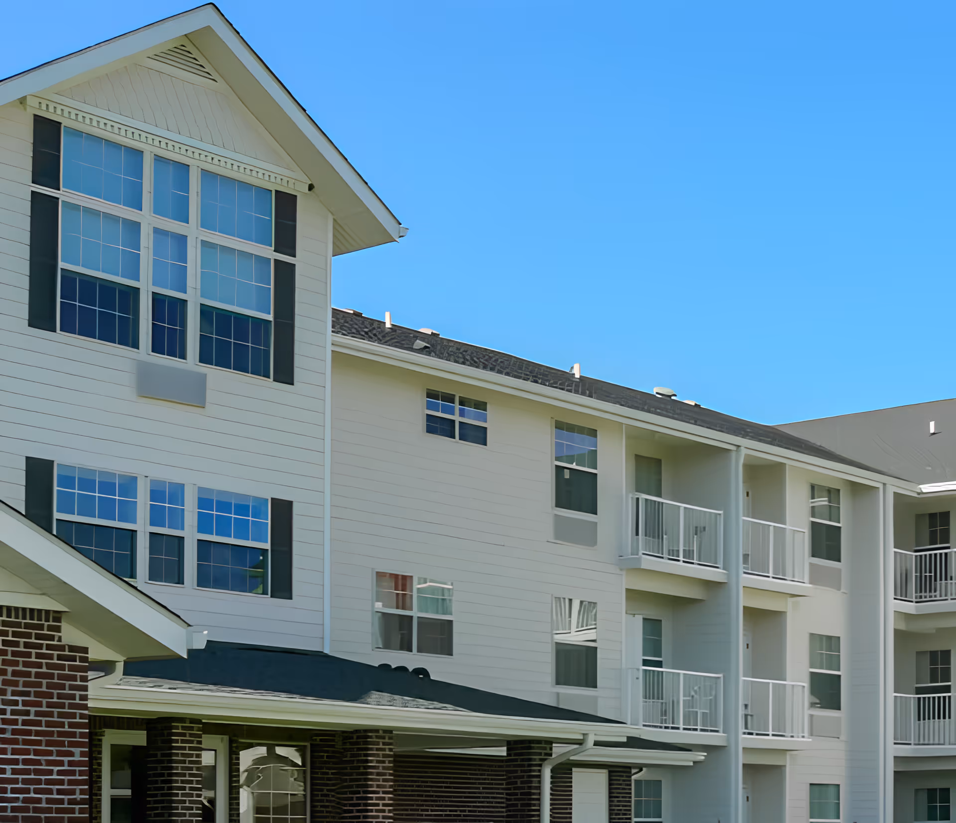 Exterior view of a multi-story senior living building with balconies and large windows under a clear blue sky.
