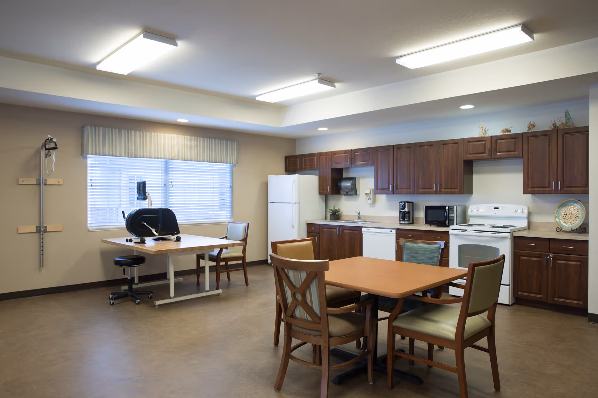 Communal kitchen and dining area with cabinets, appliances, and a central table with chairs.