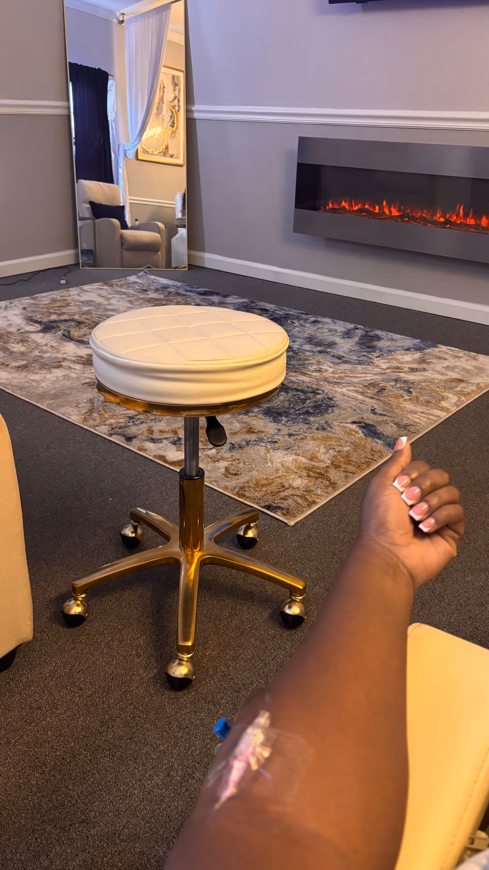 Modern senior living lounge with cream stool, rug, fireplace, and an arm visible in the foreground.