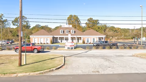 Front view of a single-story senior living facility with a sloped roof and parking lot.