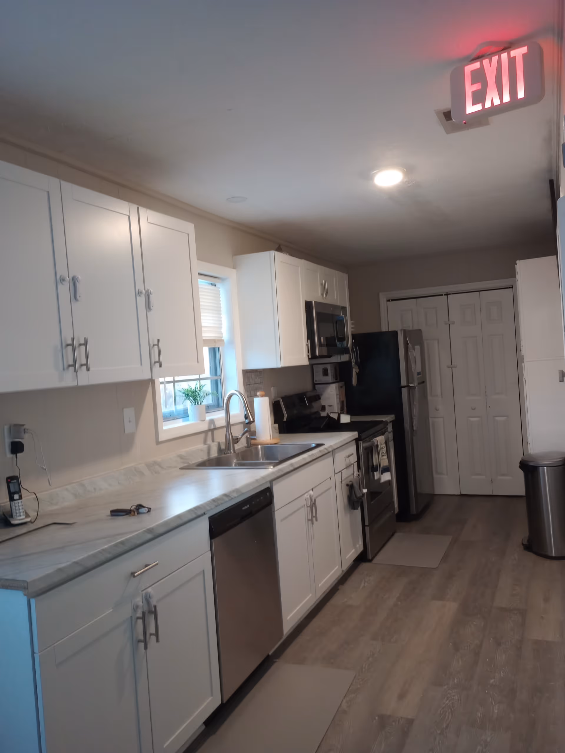 White kitchen with cabinets, stainless appliances, sink, and an exit sign.