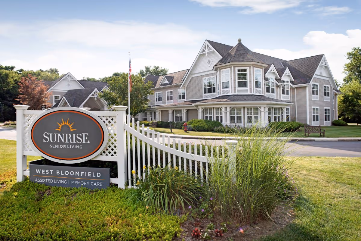Entrance sign for Sunrise Senior Living West Bloomfield in front of a large two-story senior living building and landscaped grounds.