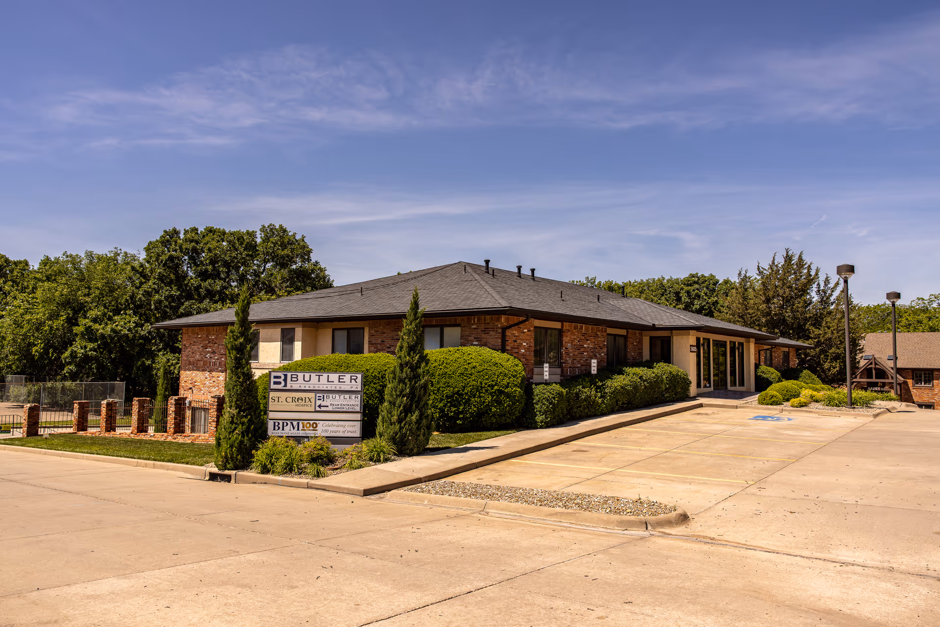 Single-story brick facility with manicured shrubs, sign, and parking lot in front under blue sky.