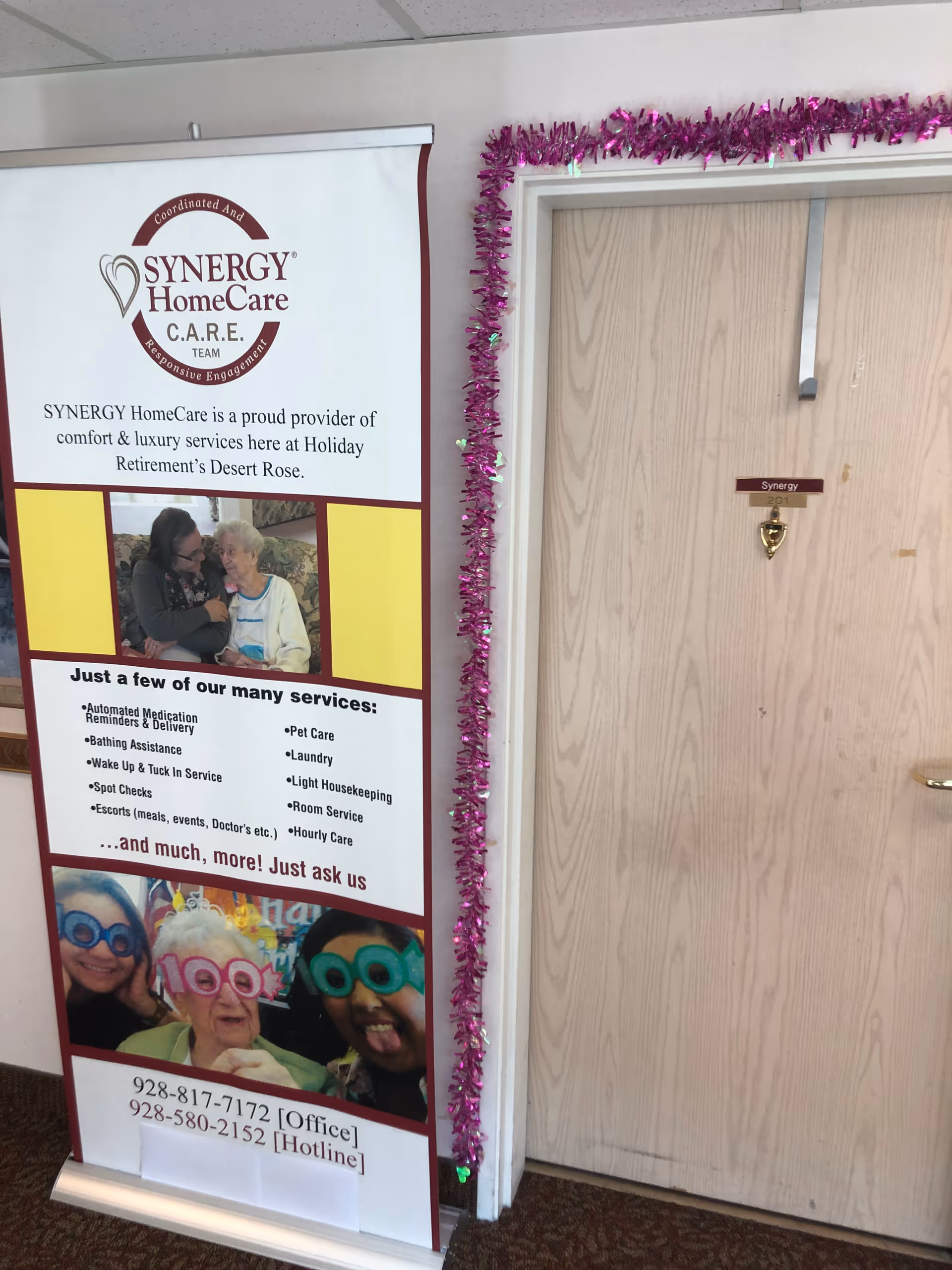 Indoor hallway with a SYNERGY HomeCare banner and purple garland around the door.