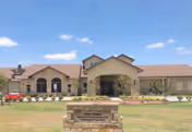Front exterior of a single-story stone-assisted living building with a central arched entrance, landscaped lawn, and a stone sign reading Arbor House Assisted Living & Alzheimer's Certified Memory Care.