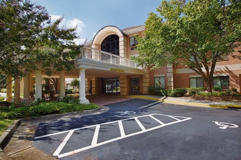 Exterior view of Independence Village of Olde Raleigh with drive-up entrance and trees.