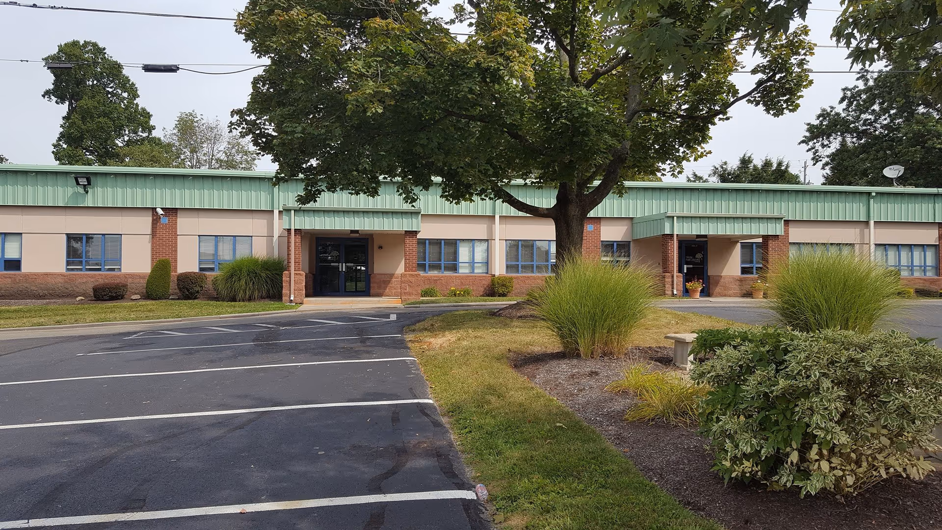 A single-story building with green trim, brick accents, and a parking lot in front.