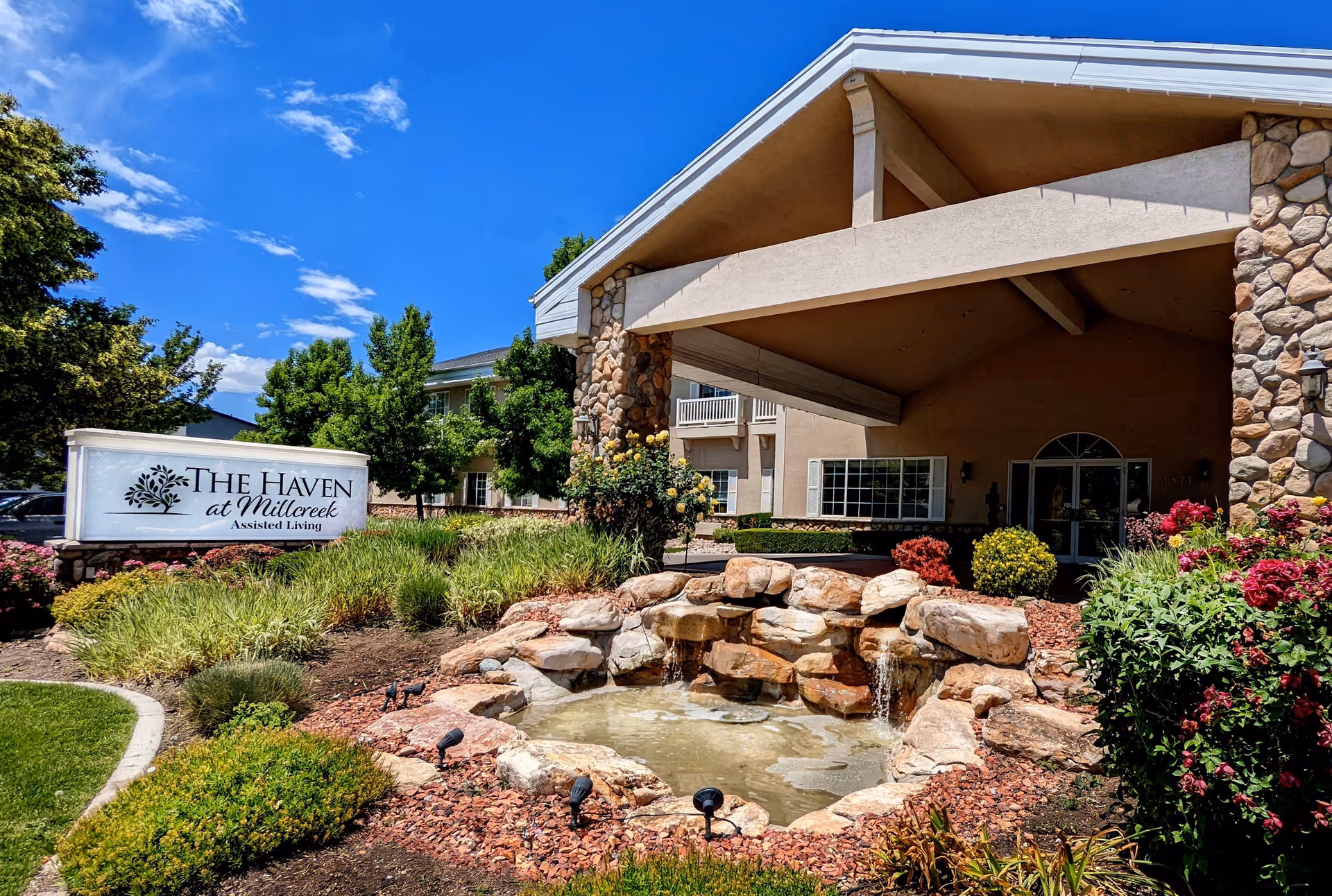 Exterior view of The Haven at Millcreek entrance with stone columns, garden, and small waterfall.
