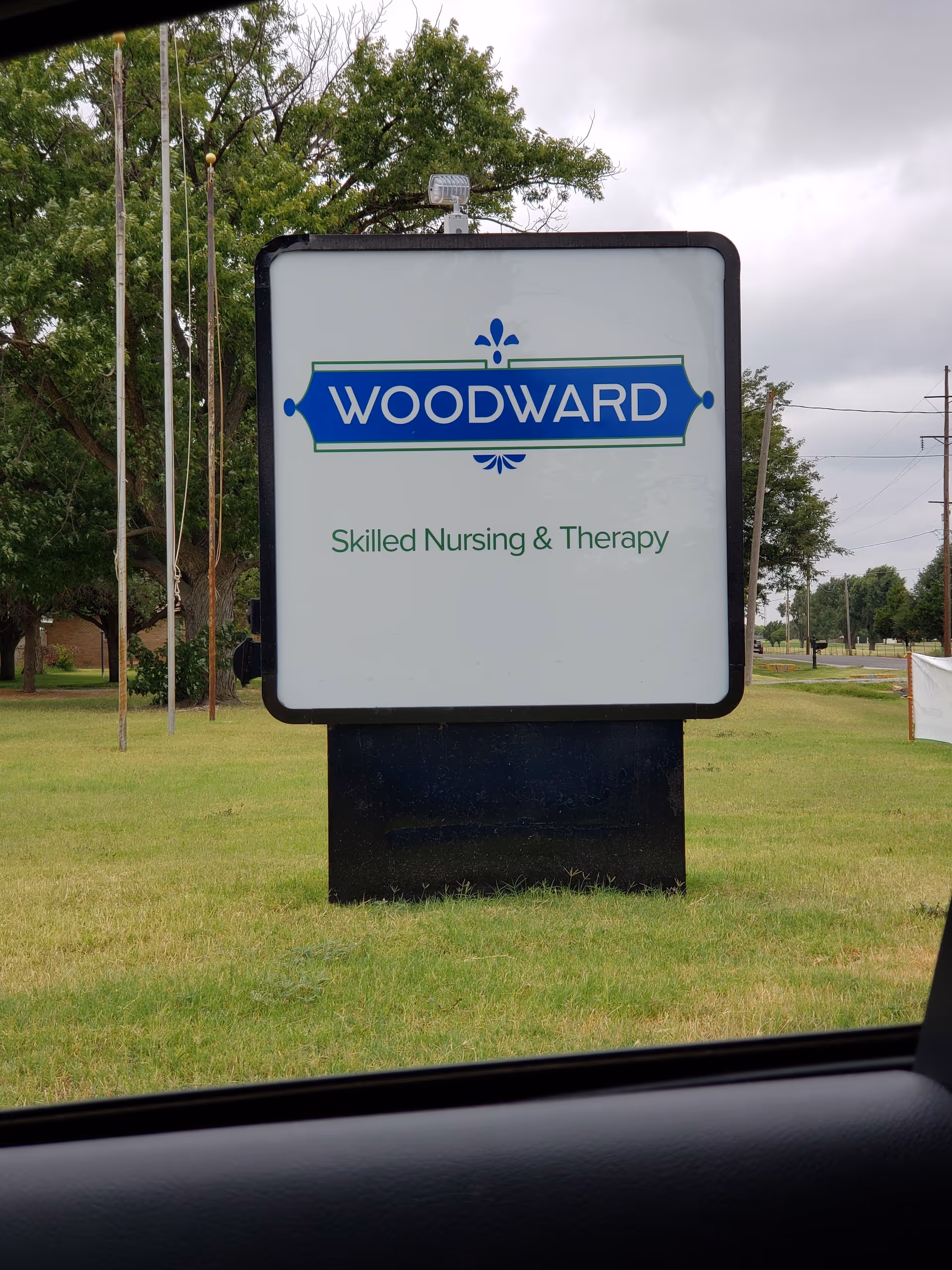 Large Woodward Skilled Nursing and Therapy sign on a grassy lot, viewed from a car.