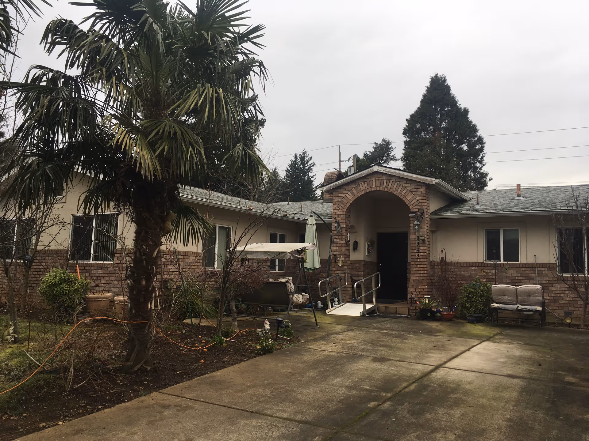 Single-story beige-brick senior care facility exterior with arched entrance and seating.