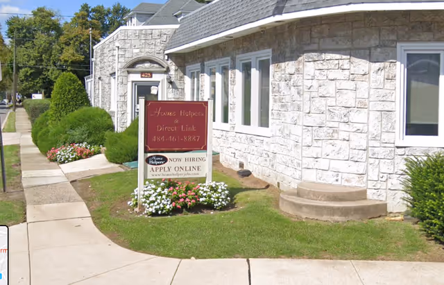 Stone-faced senior living facility exterior with a sign and flower beds by the sidewalk.