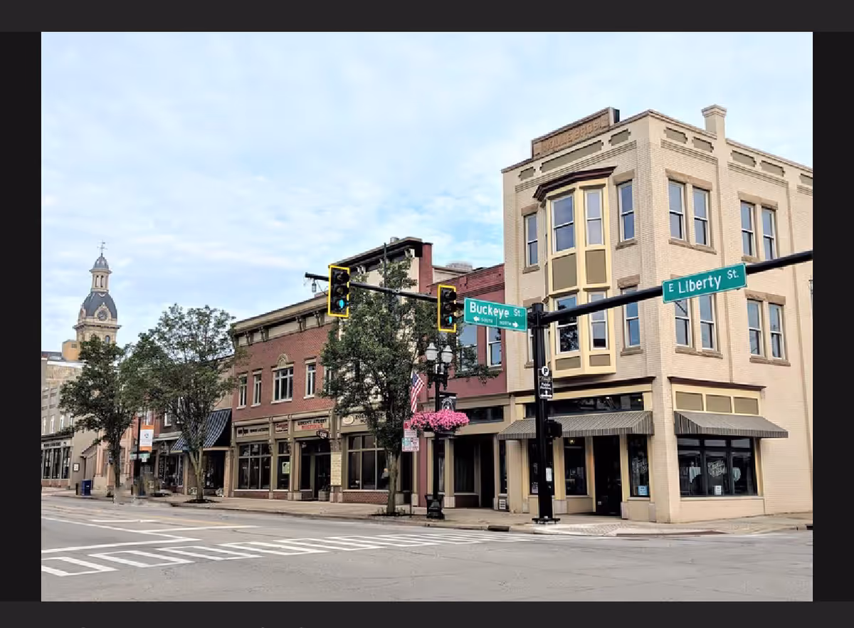 Downtown street corner with brick storefronts, traffic lights, and Buckeye and Liberty street signs.