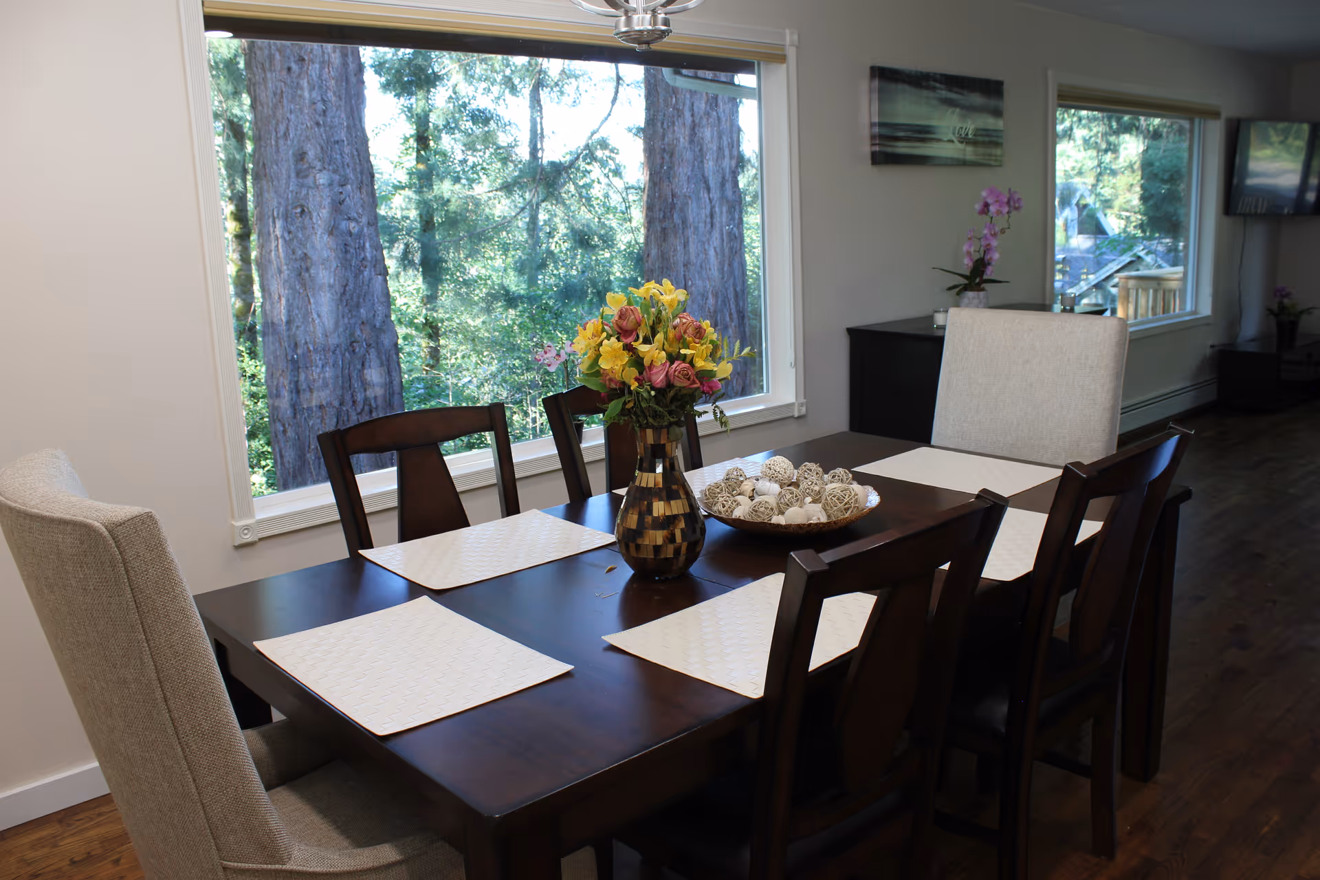 A dark wooden dining table with six chairs and decorative centerpiece in a bright dining area.