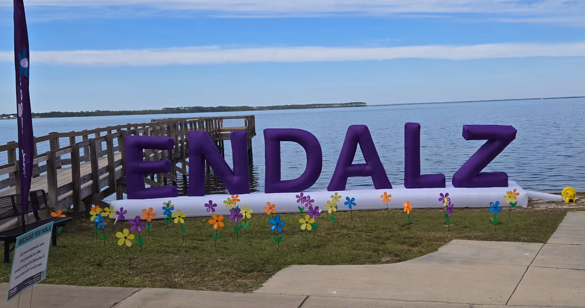 Large purple ENDALZ letters along a waterfront with a pier and colorful flower decorations.