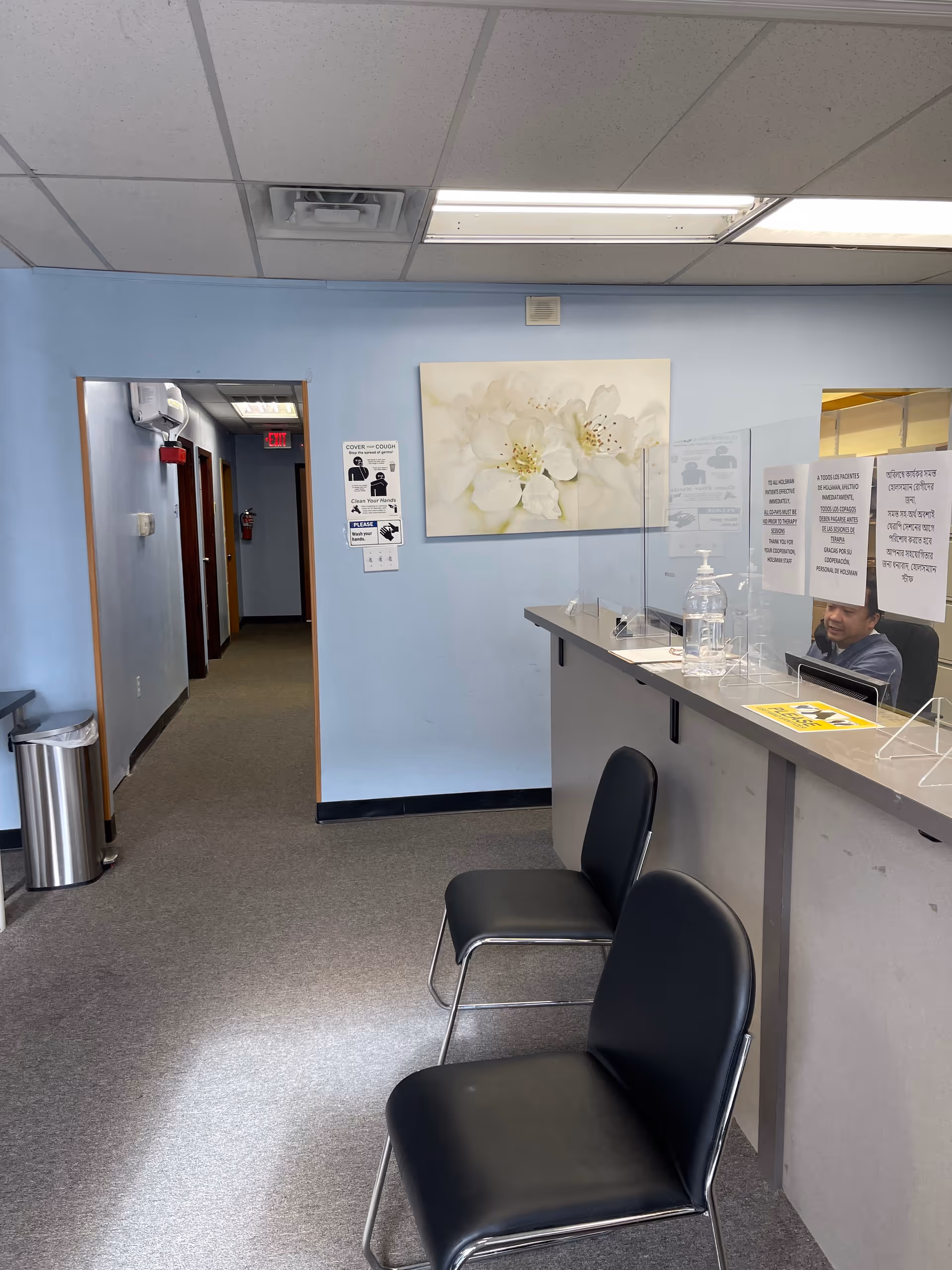 Reception area with two black chairs and a front desk in a light blue hallway.