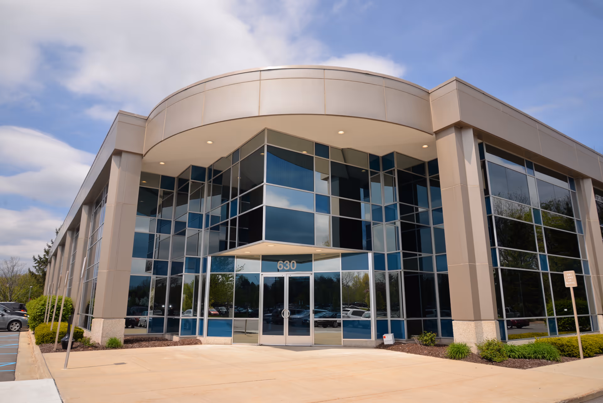 Modern glass-front building with curved entrance and large windows against a blue sky.