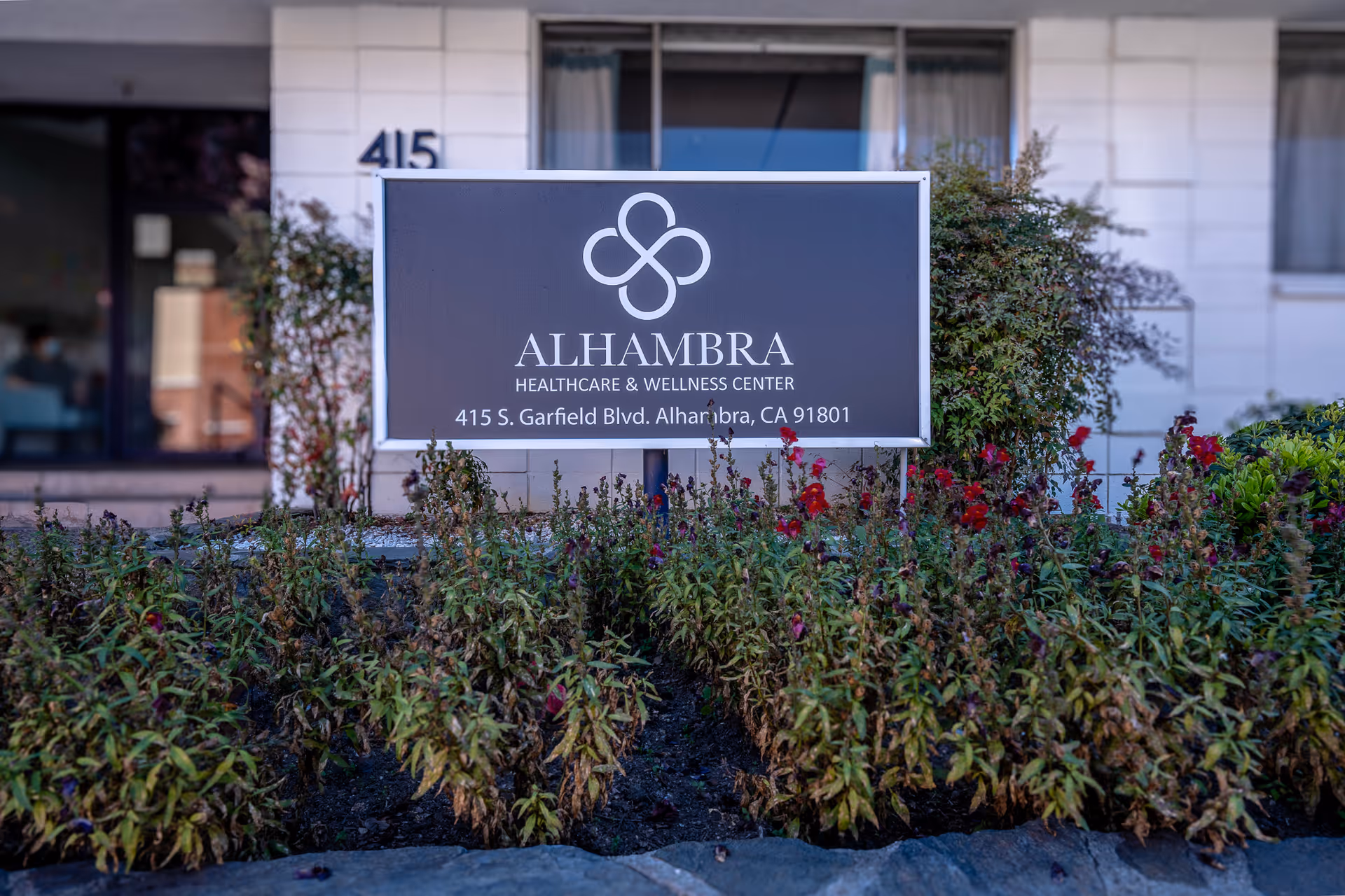 A freestanding sign reading "Alhambra Healthcare & Wellness Center" sits in landscaped beds in front of the facility's facade.