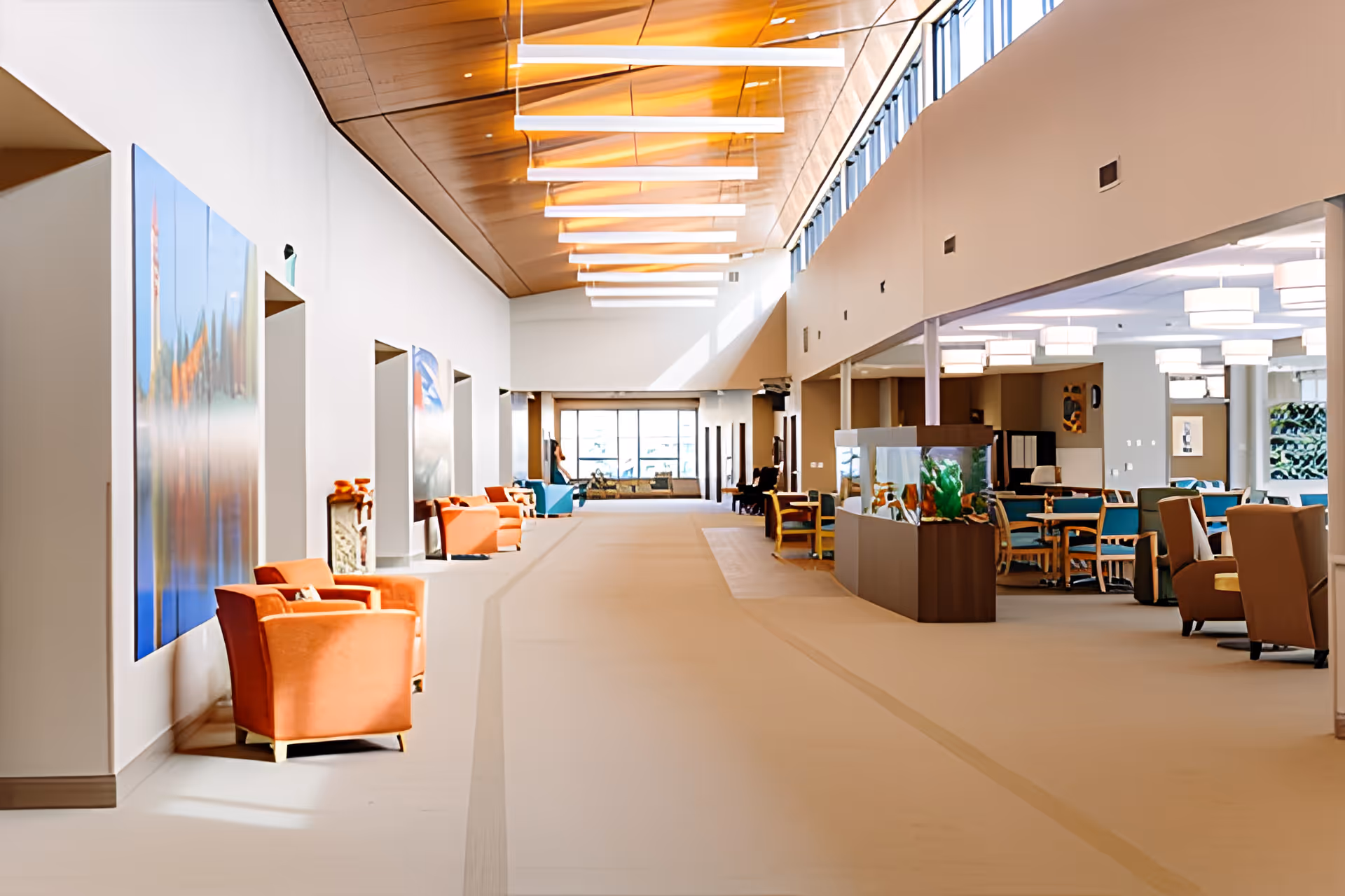 Bright modern senior living community common area with seating, tables, and an aquarium under a high wooden ceiling.
