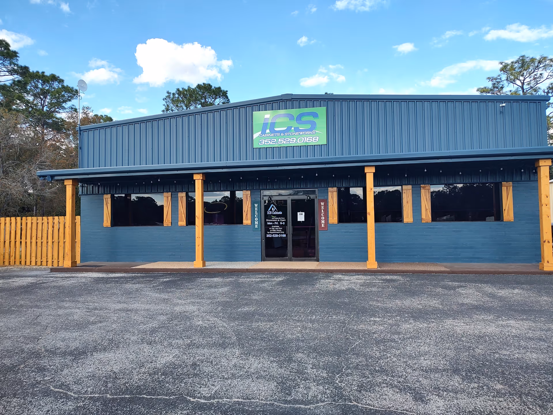Blue industrial building storefront with ICS Cabinets sign, wooden pillars, and glass doors