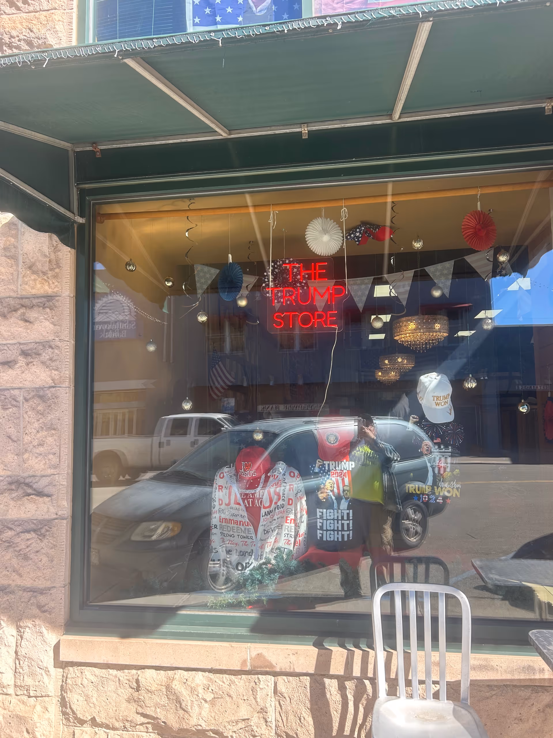 Storefront window displays The Trump Store sign, patriotic decorations, and assorted merchandise through glass.