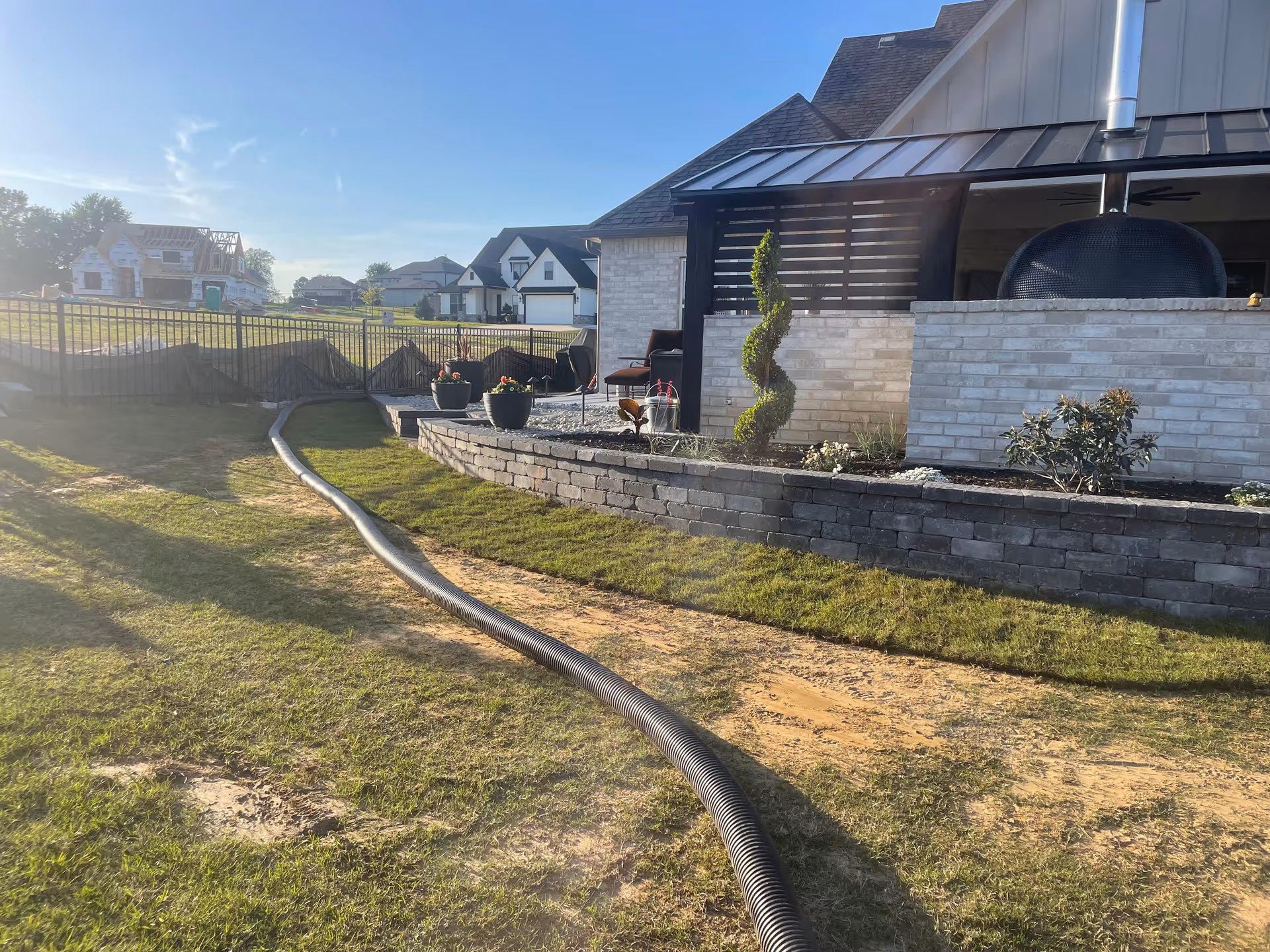 Outdoor patio at Oxford Glen at Owasso with brick wall, potted plants, and a long hose.