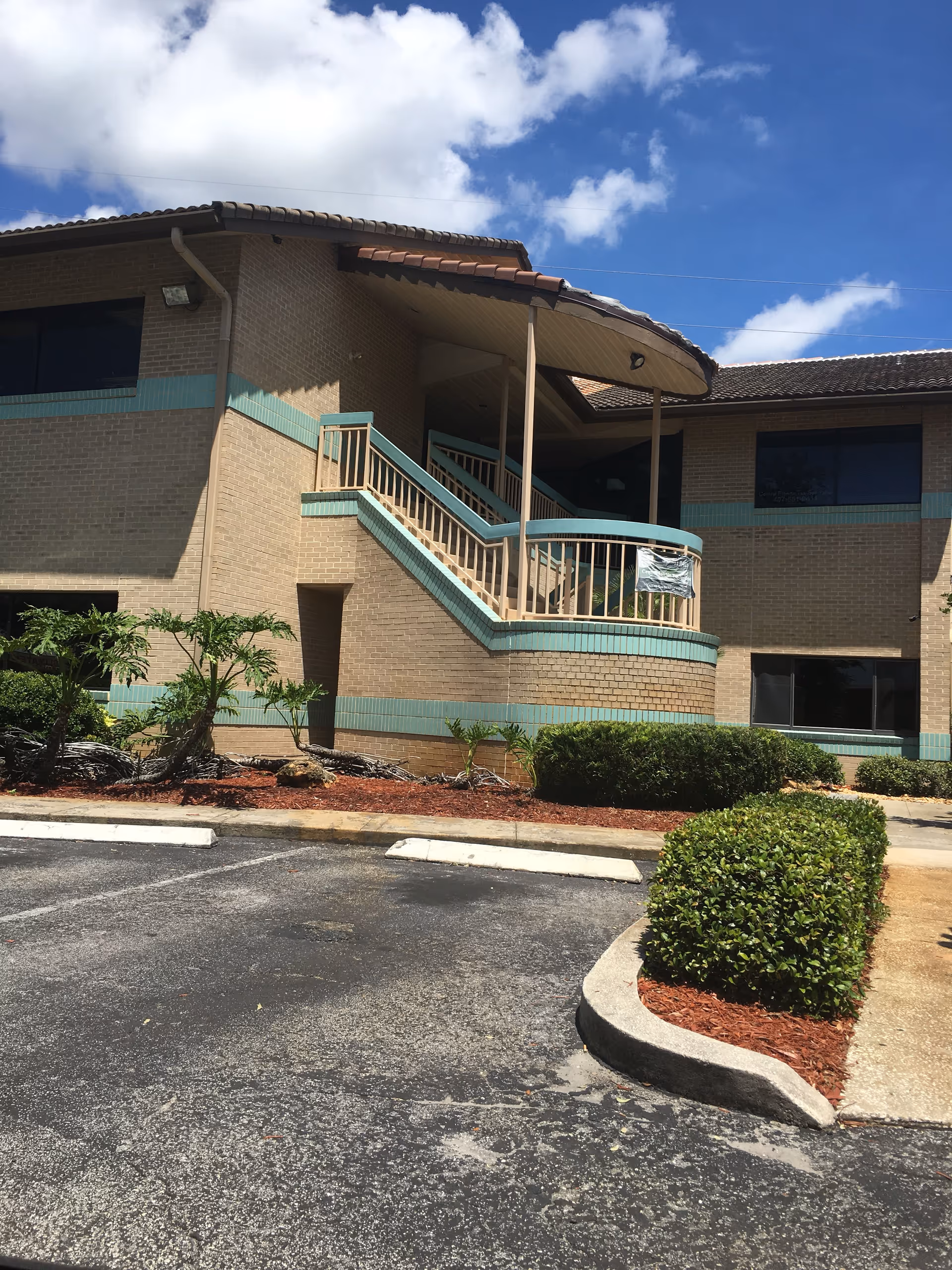 Exterior view of a brick senior facility with a curved teal staircase entrance.