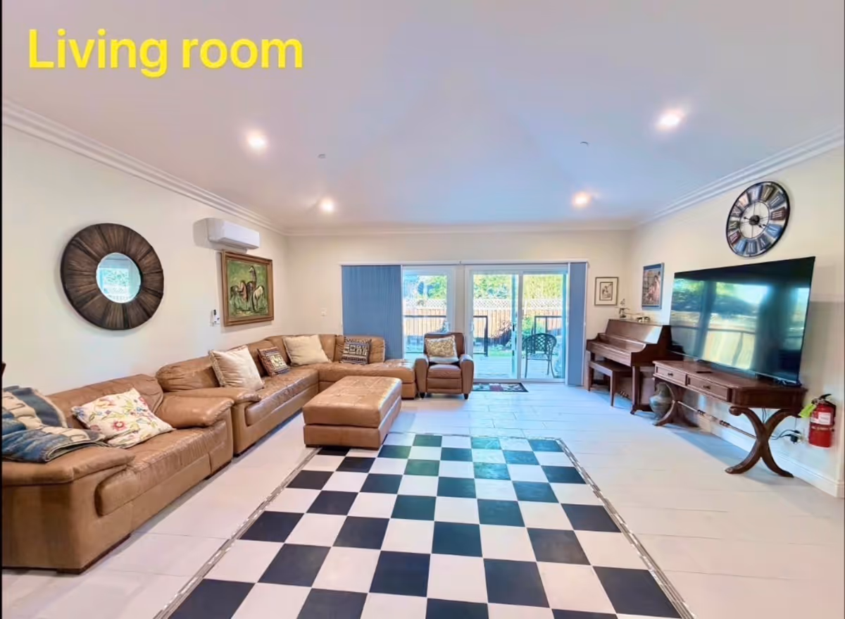 Spacious living room with brown sectional, checkered rug, piano, and sliding glass doors.