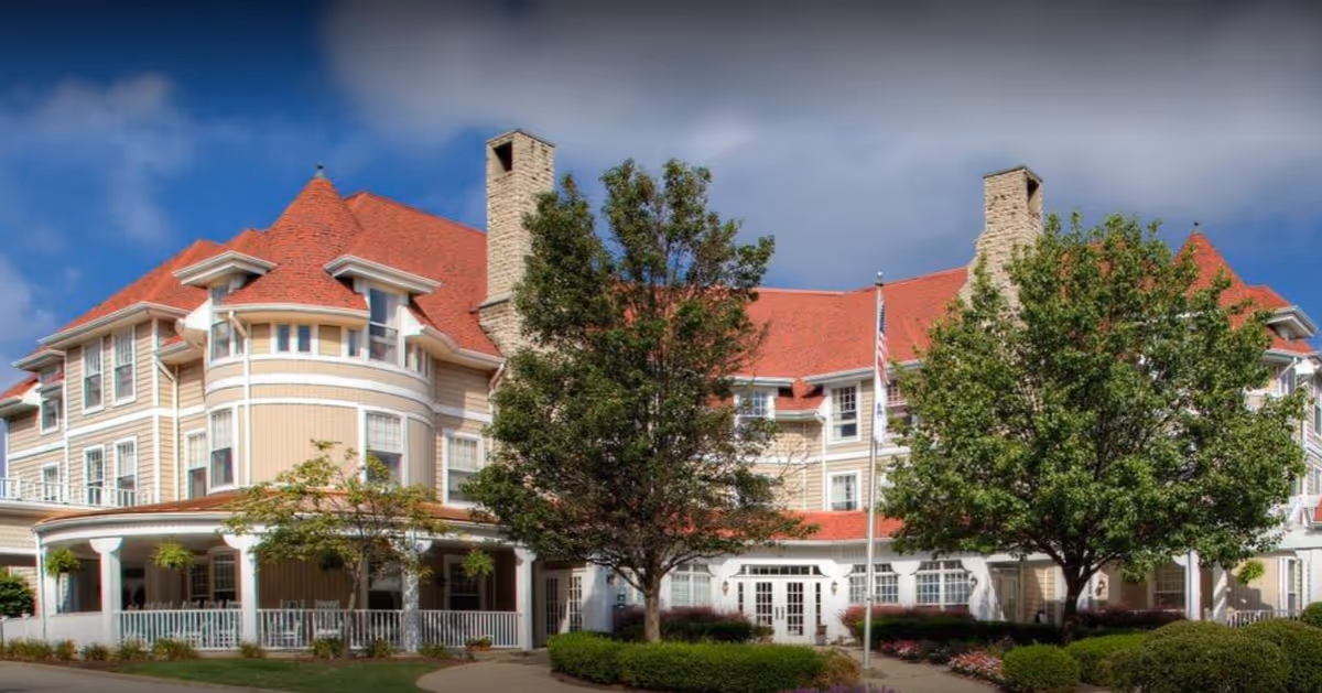 Senior living facility with red roof and white siding, surrounded by trees and a flag.