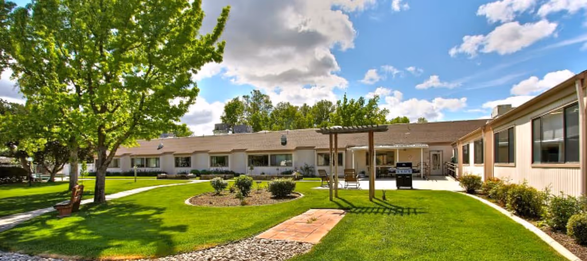Outdoor courtyard of Skyline Transitional Care Center with green lawn, trees, and benches.