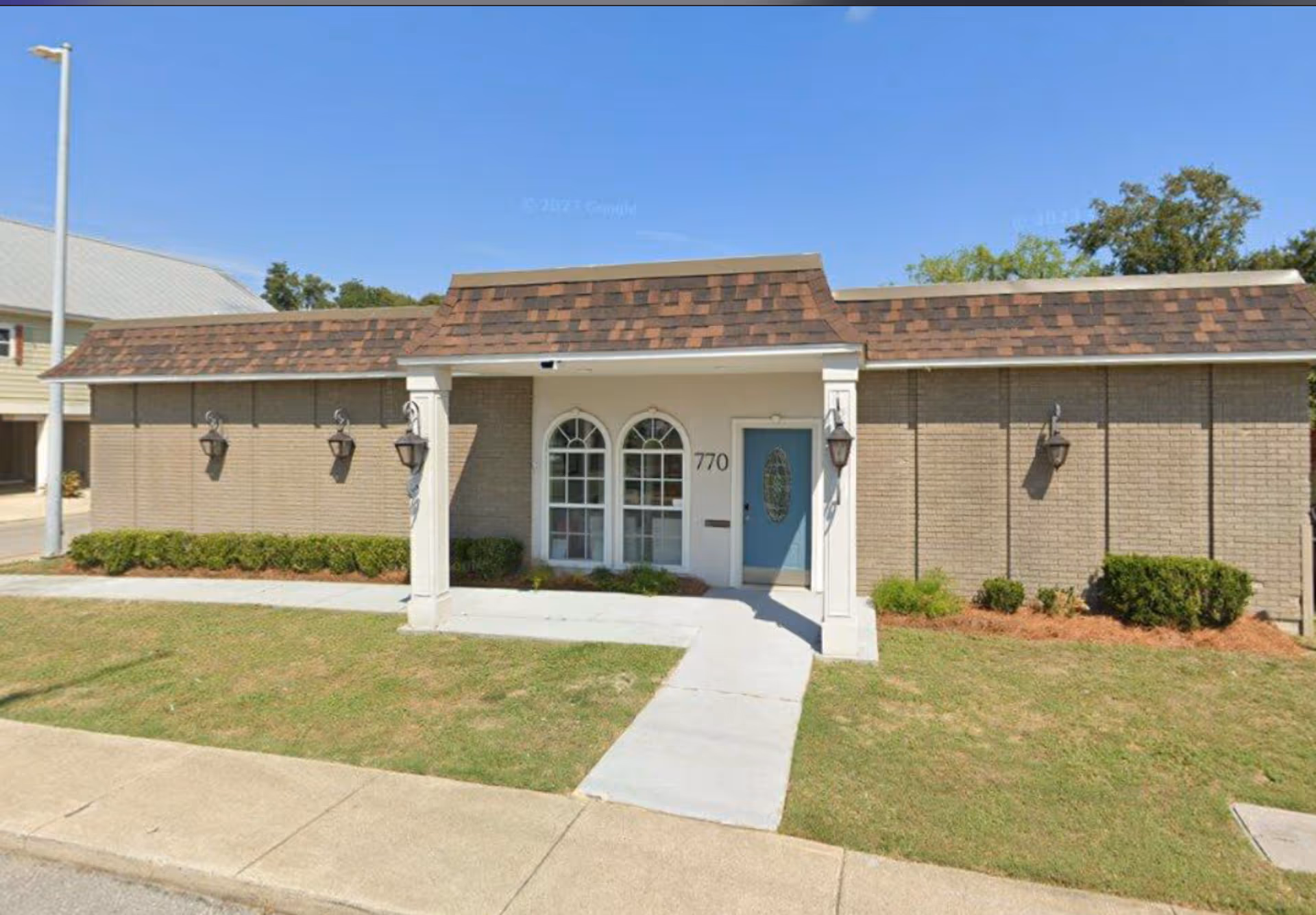 Exterior of a single-story brick facility with arched windows and a blue front door.