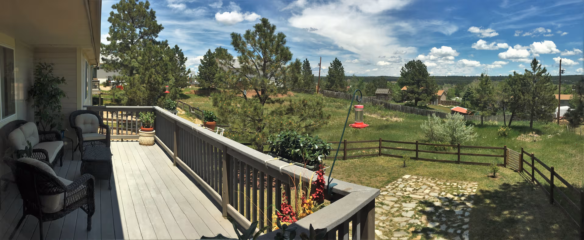 Outdoor balcony with seating overlooks a green, tree-filled rural landscape.