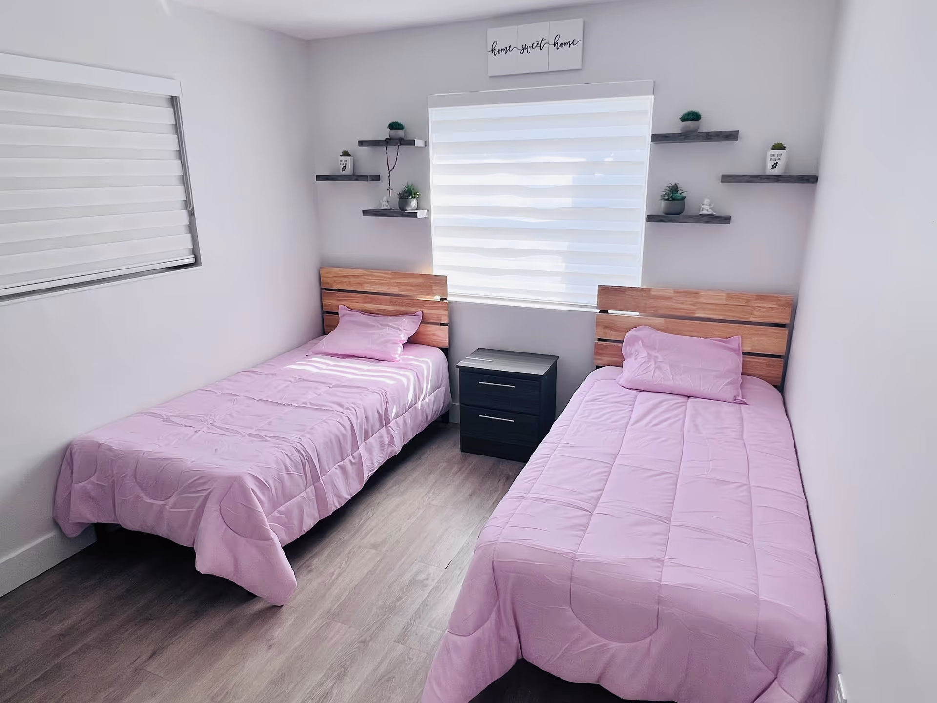 Two single beds with lavender quilts in a small bedroom with a nightstand.