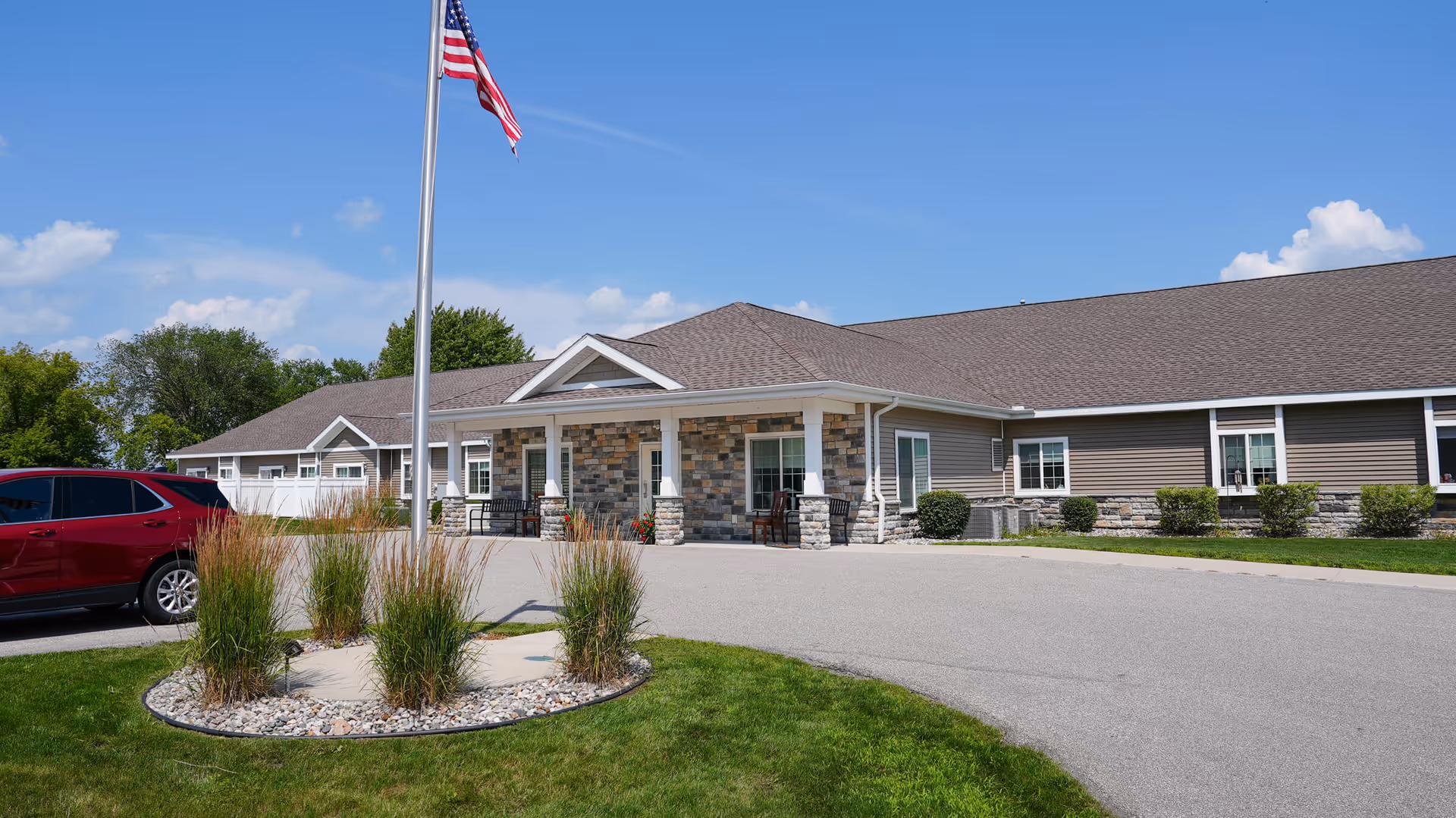 Exterior view of Merrill Fields Assisted Living building with flagpole, circular landscaping, and parking.
