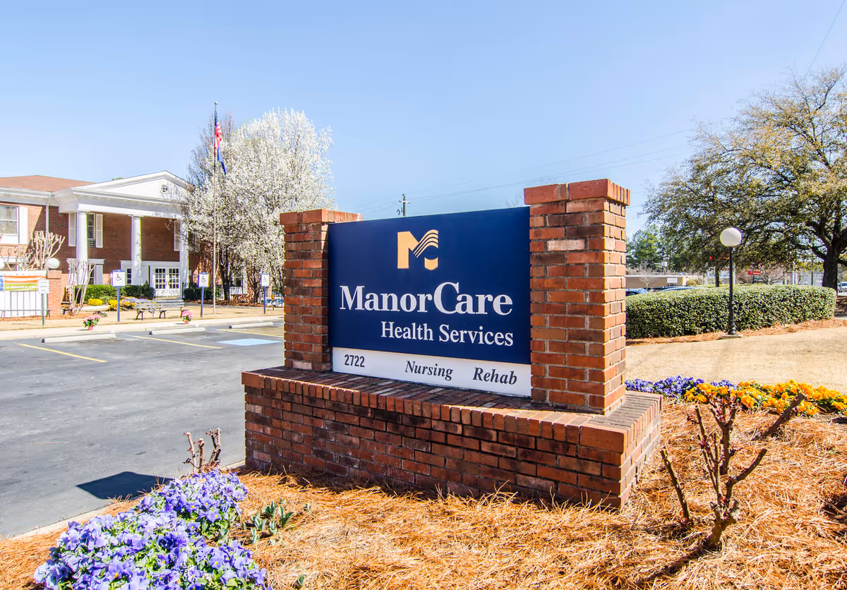 Blue ManorCare Health Services sign in brick planter at the facility entrance.