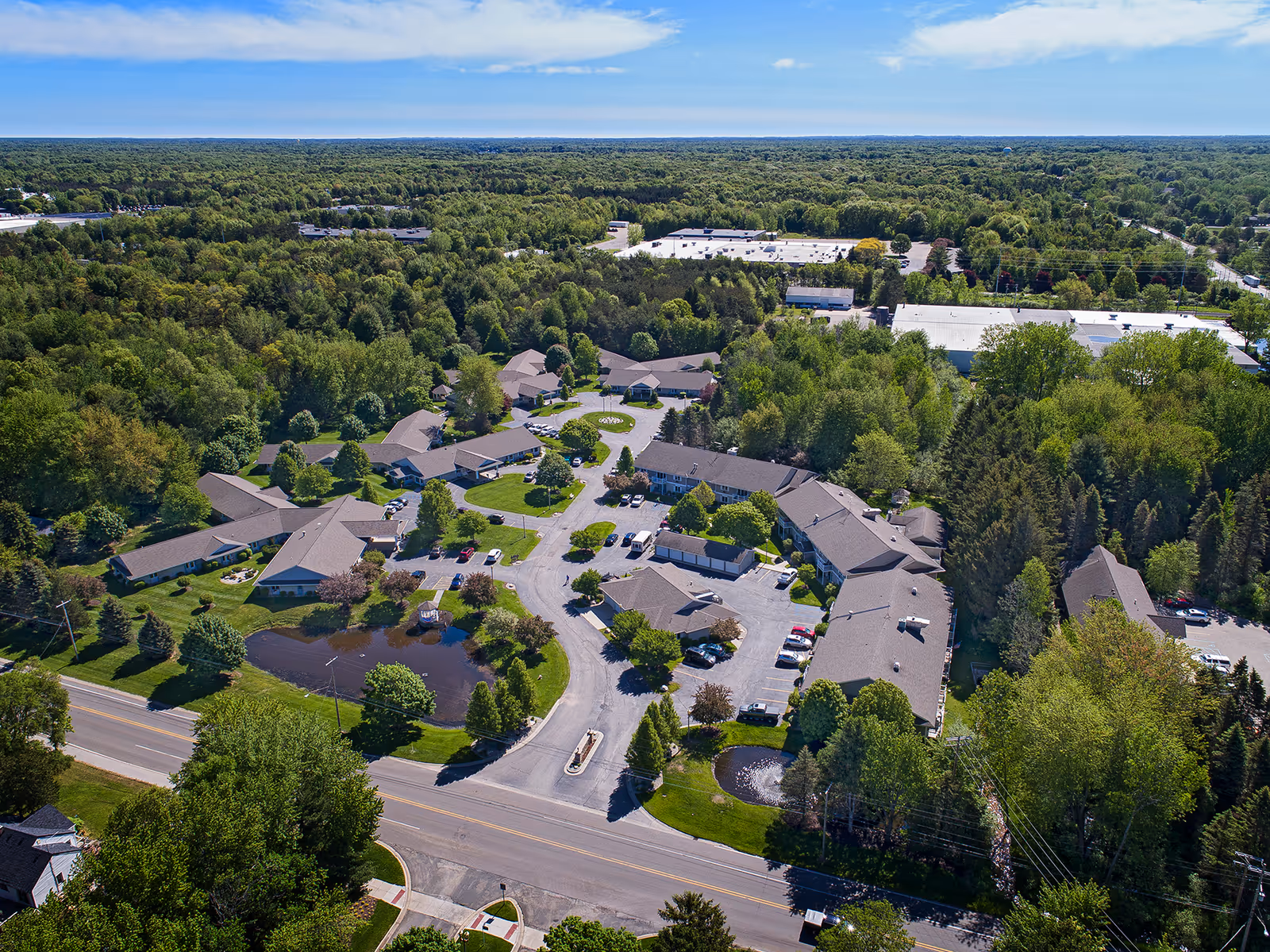 Aerial view of a multi-building senior living campus surrounded by trees, parking, and a pond.