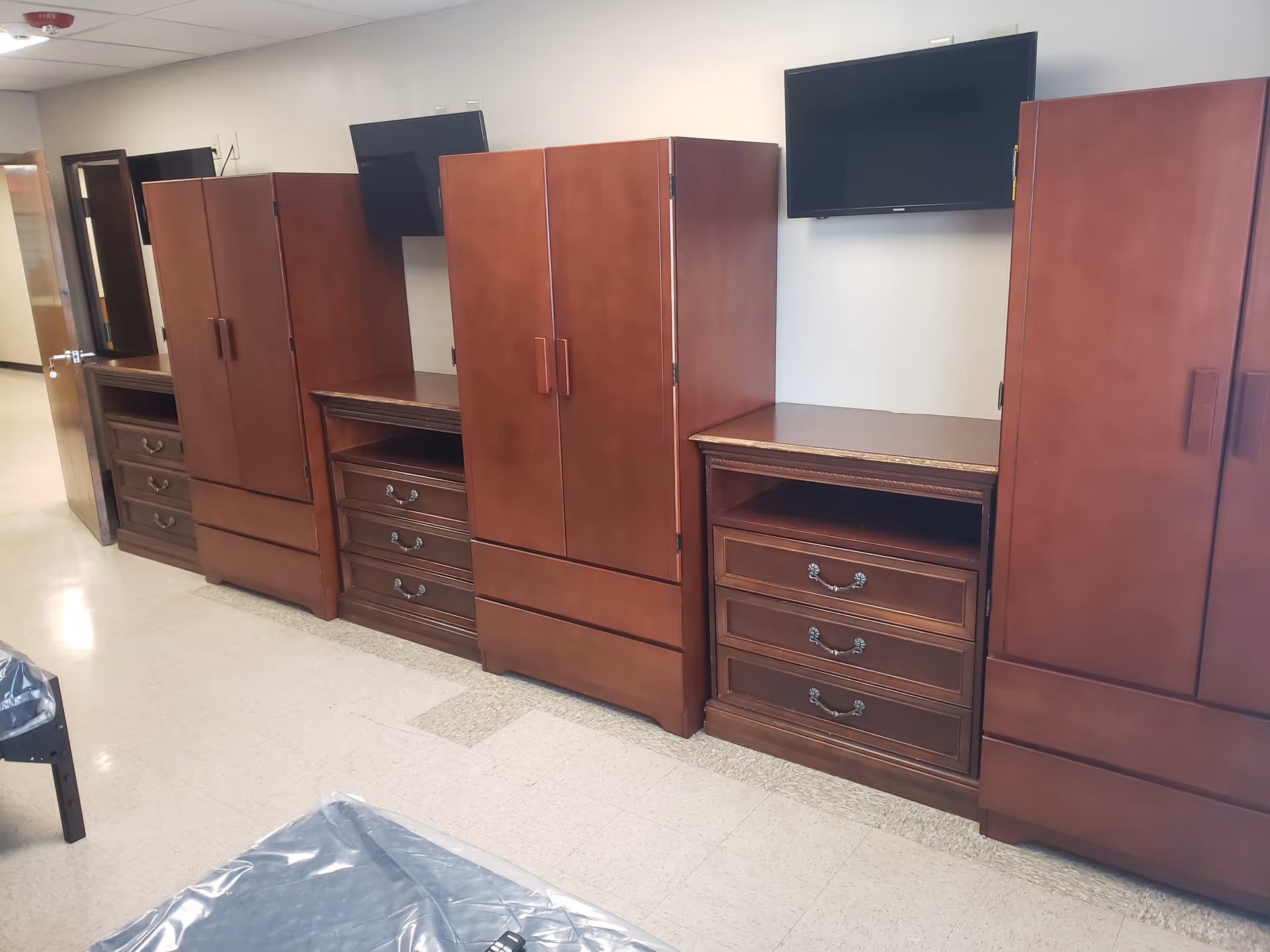 Row of dark wood wardrobes and dressers with wall-mounted TVs.