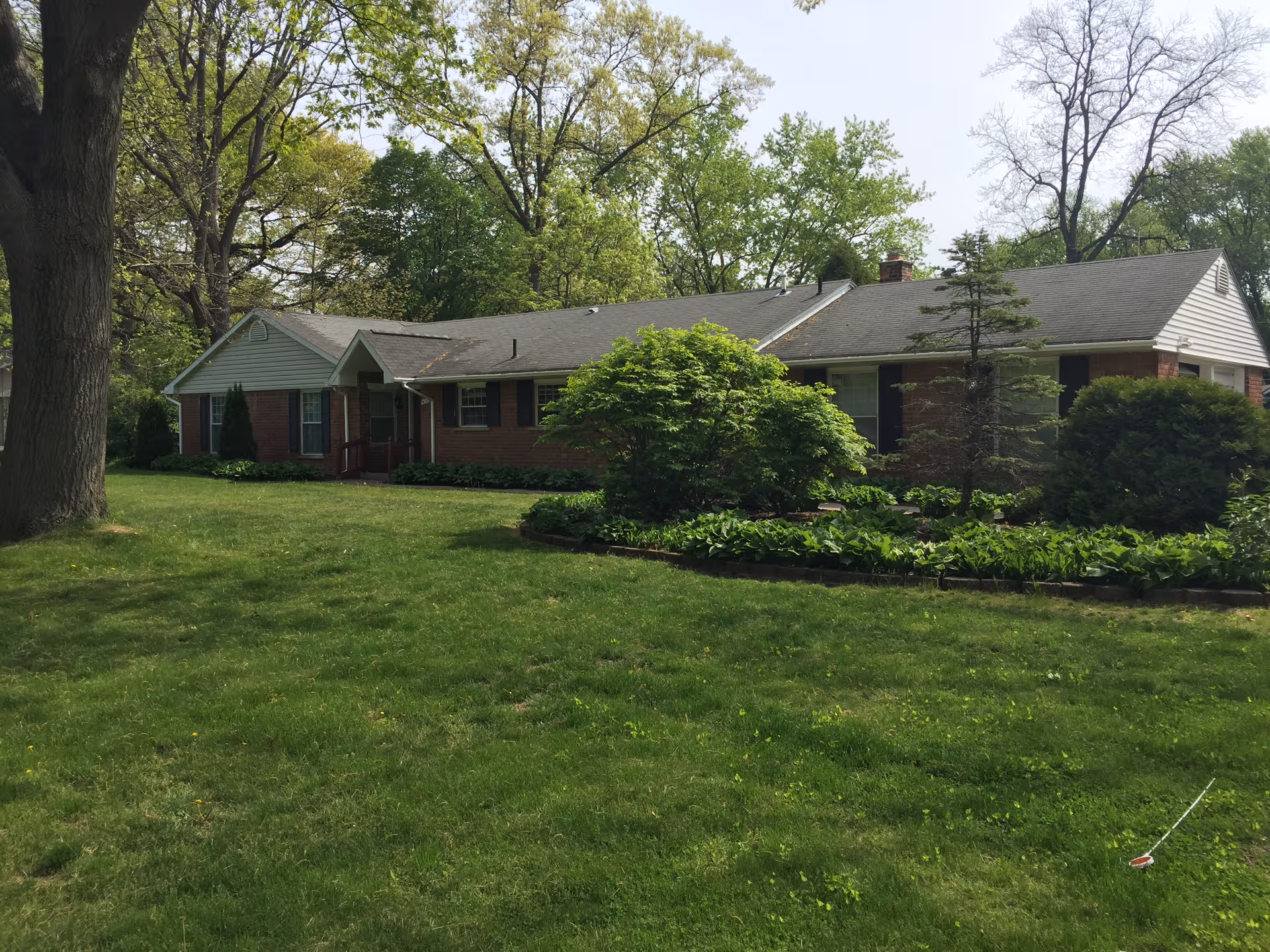 Brick single-story senior care home with green lawn, shrubs, and tall front-yard trees.