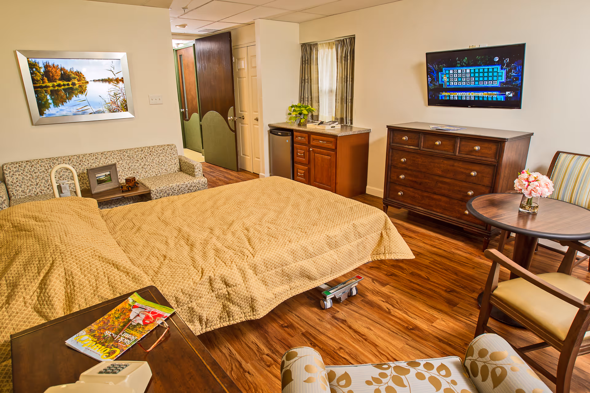 Cozy hotel-style bedroom suite with a bed, sofa, dresser, TV, and round table.