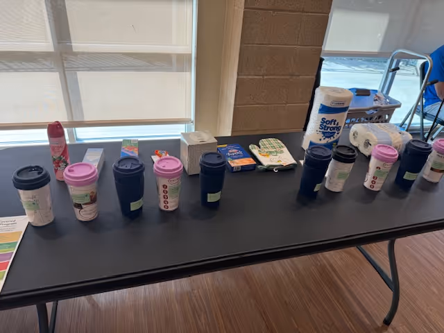 A long table displays assorted travel mugs, packets, and supplies near bright windows.