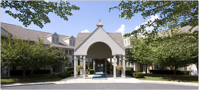 Exterior view of Carrington Place Apartments senior living facility entrance with archway and landscaped grounds.