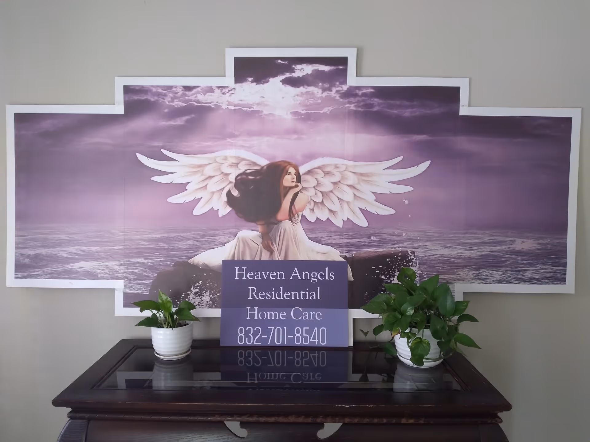 Purple angel wall art above a console table with a Heaven Angels sign and plants.