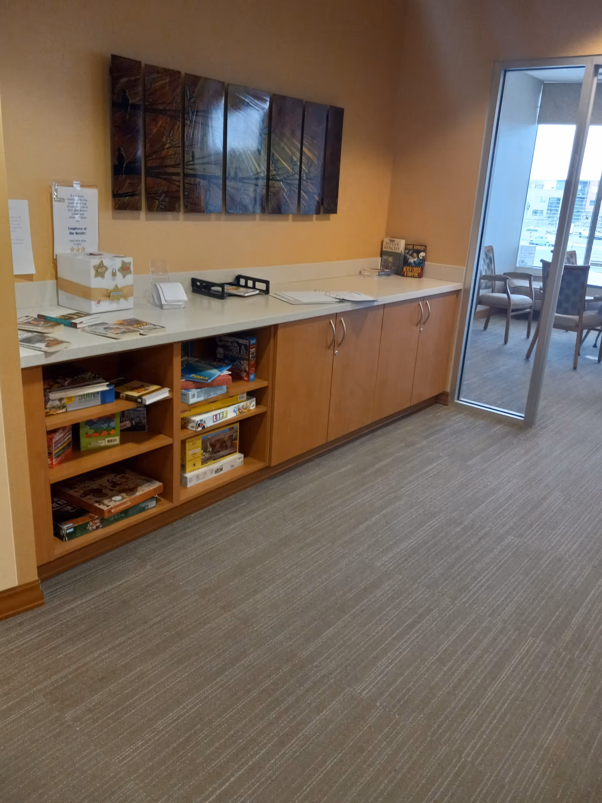 A hallway with long counter, cabinets, board games, and a glass door to a seating area.