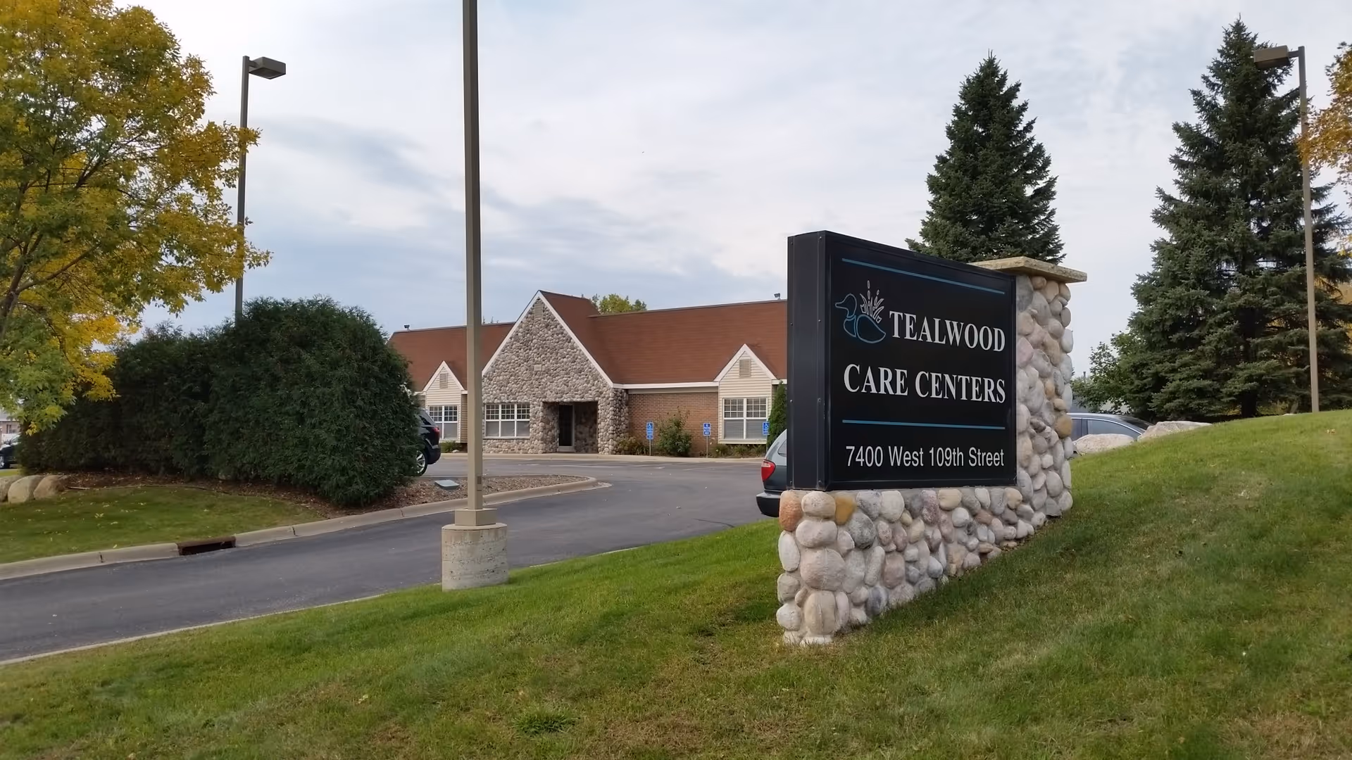Exterior view of a Tealwood Care Centers building with a stone sign and parking lot.
