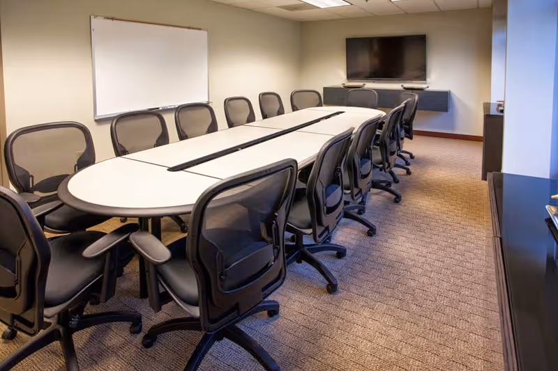 Modern conference room with long oval table, many chairs, a whiteboard, and wall-mounted TV.