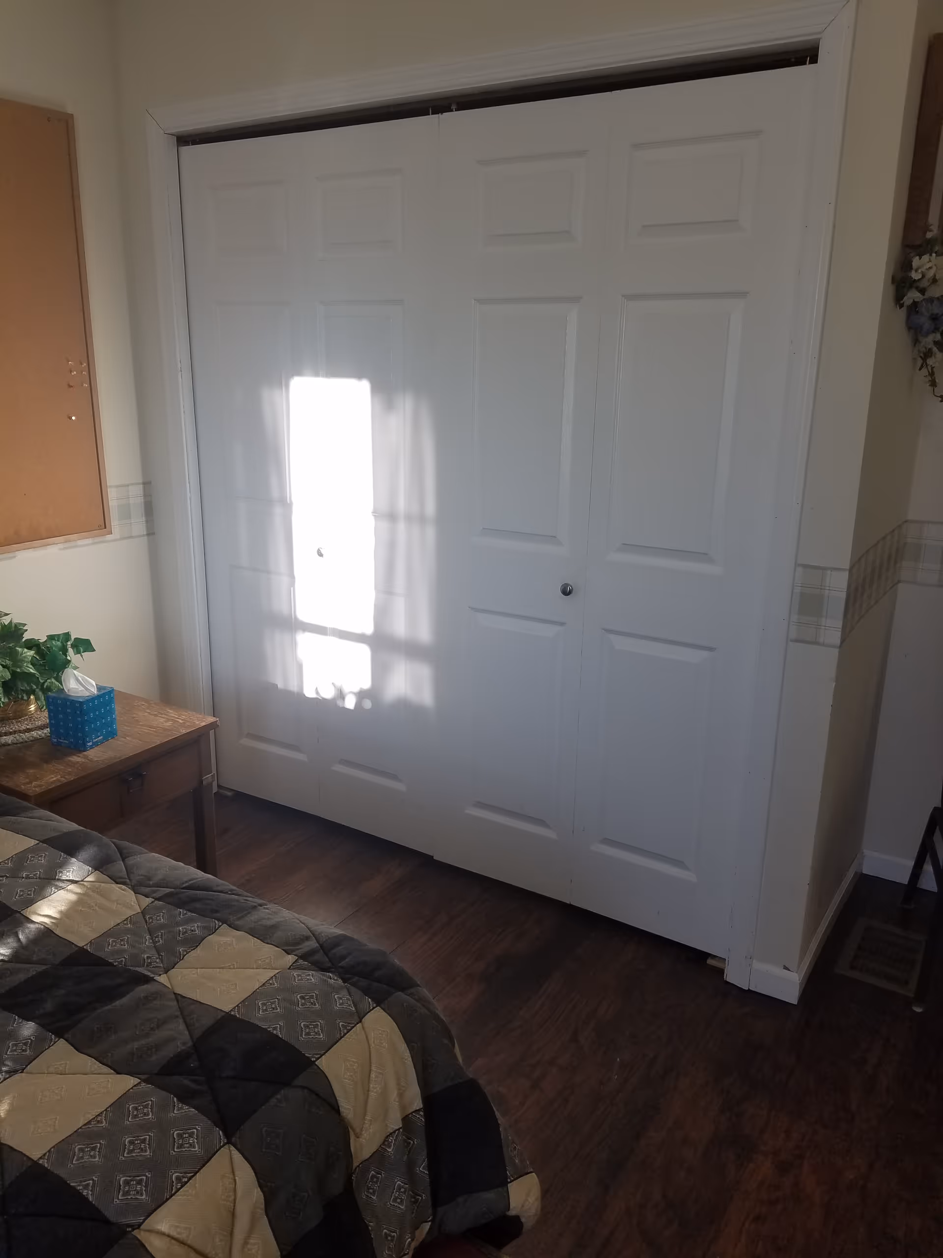 White double closet doors dominate, with a quilted bed and nightstand in a bedroom.