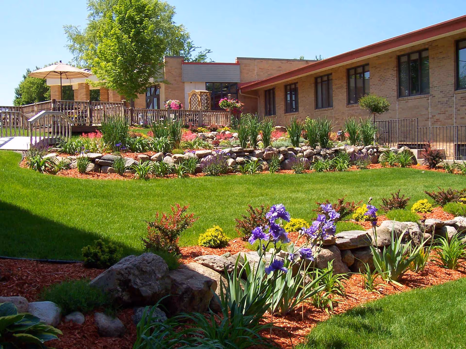Well-kept outdoor garden with flowering beds and a brick senior care facility.