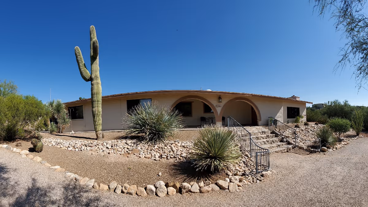 Single-story building with arched entryways amid desert landscaping and a tall cactus.